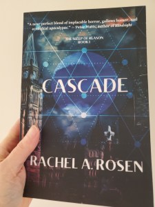 A woman's hand is holding a copy of the novel Cascade by Canadian author Rachel A. Rosen. The cover features a blue sphere hovering over the Ottawa parliament building.